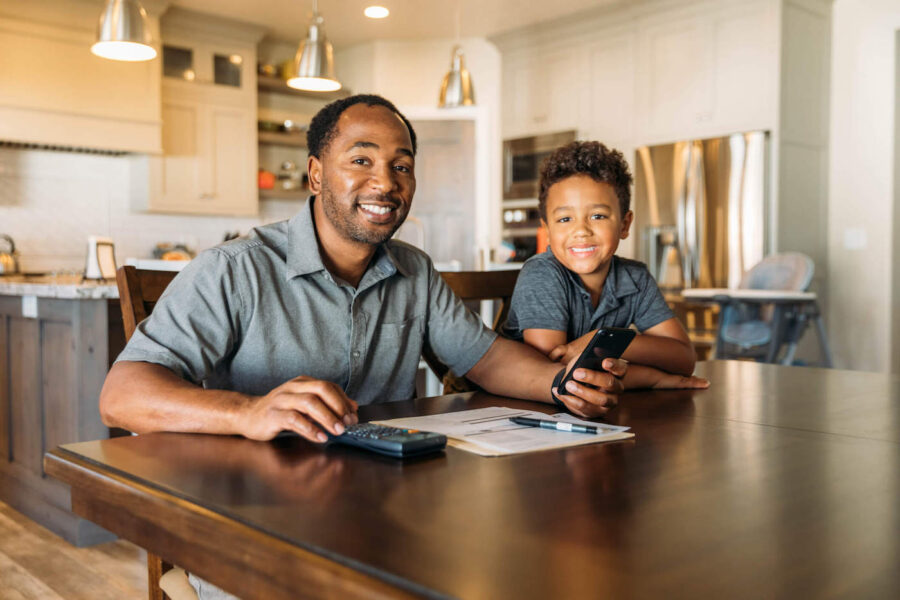 A middle-aged man sits at his dining room table with his young son teaching him about home finances.