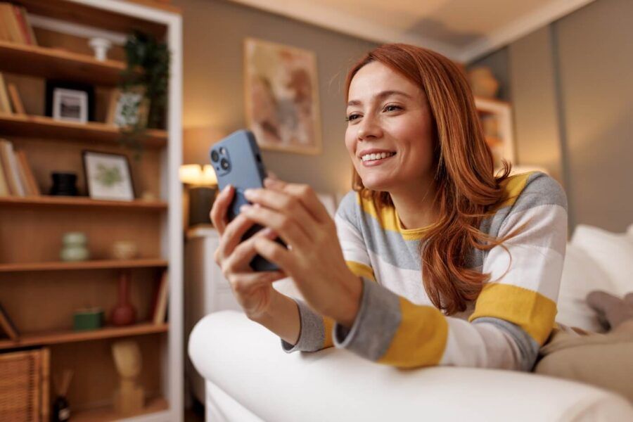 Smiling woman relaxing on a couch with a smartphone