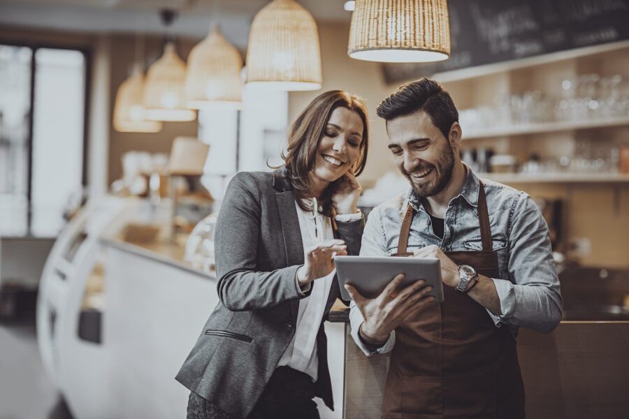 Shot of a smiling cafe owner and employee barista standing inside a coffee shop looking at a digital tablet.