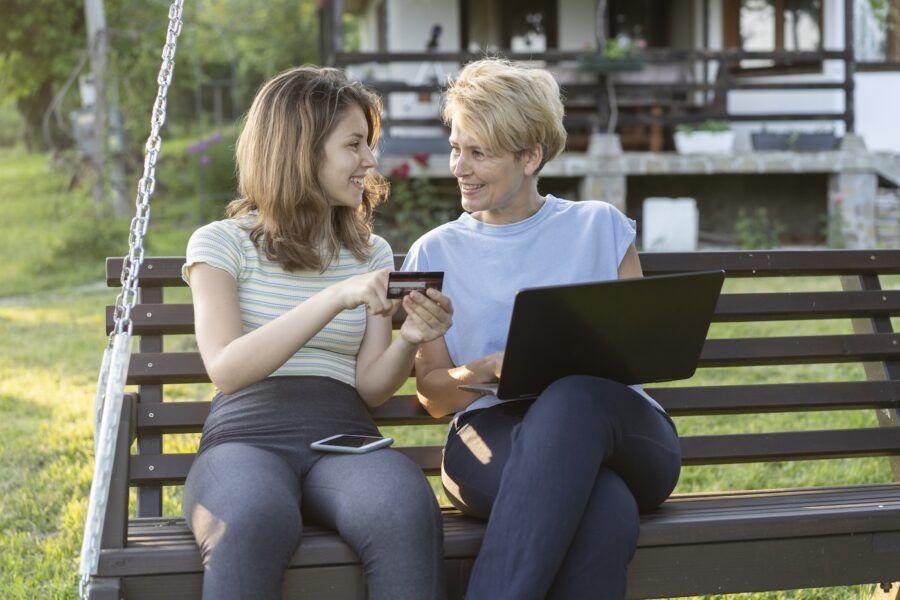 Mother and daughter sitting at porch swing and buying online with a credit card.