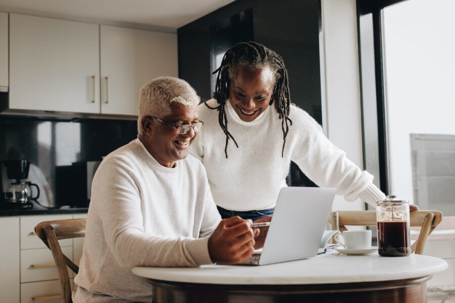 Retirement planning at home. Cheerful senior couple smiling happily while looking at a laptop screen. Happy mature couple researching their retirement options together.