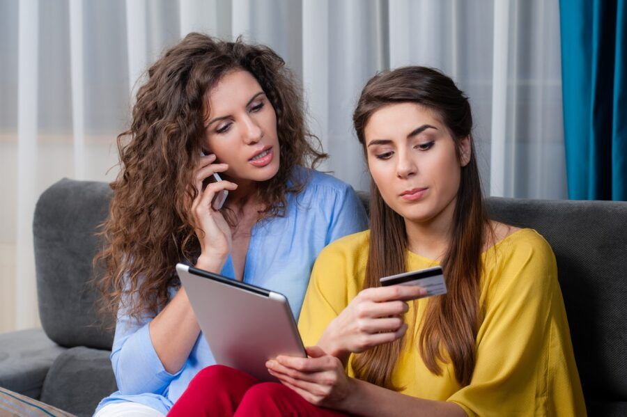 Two woman sitting at home in the couch talking about credit cards.