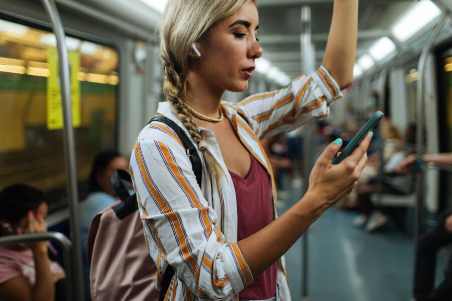 Young blond woman standing in a subway train while using a digital wallet on her cellphone
