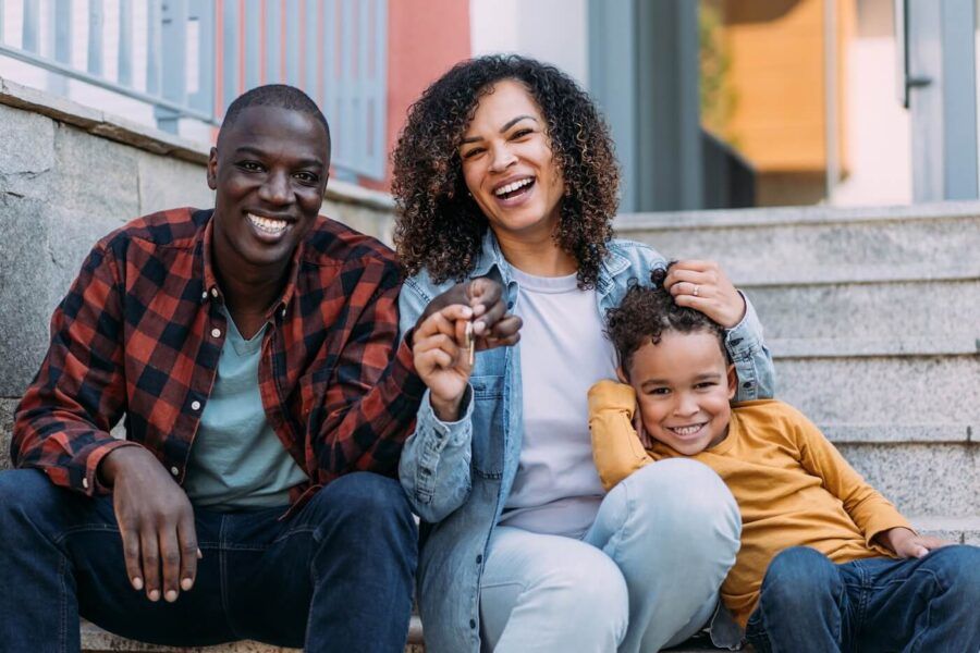 Happy family of three sitting on the porch of their new house and holding the keys