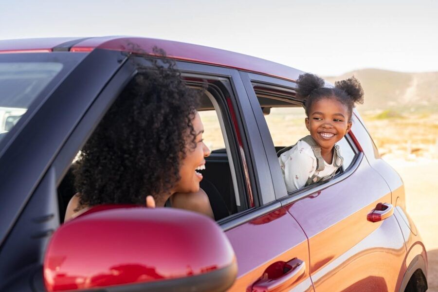 Young smiling girl and her mother popping out of the car window