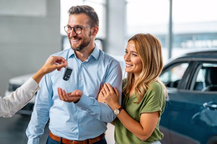Happy couple taking the car keys from the dealership agent