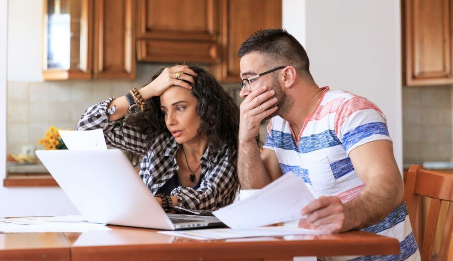 A man and a woman sitting at home and working on home finances, stressed about potential fraud.