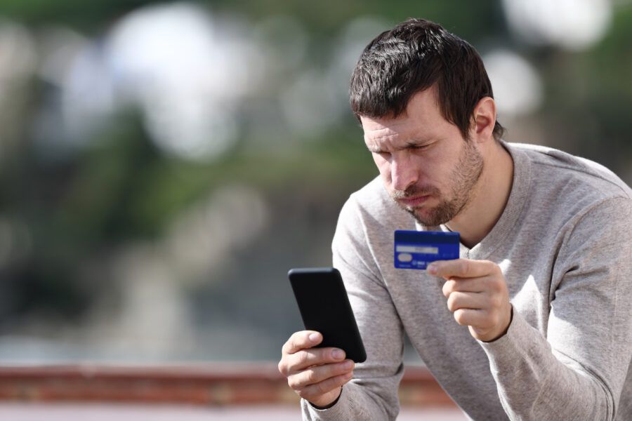 Worried man avoiding credit card cancellation, holding credit card and phone