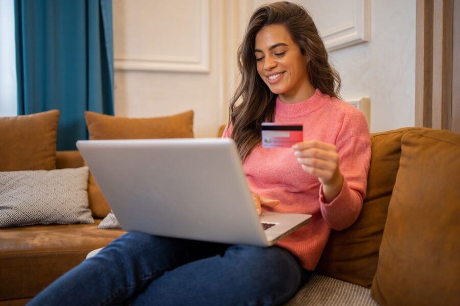 Smiling young woman using her credit card for online shopping at home