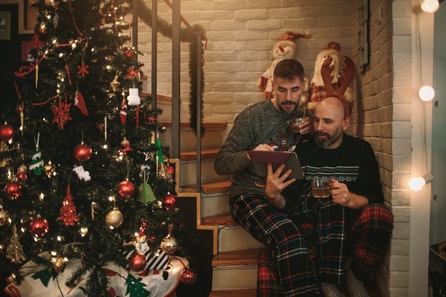 A couple sitting on their stairs and online shopping using buy now, pay later on digital tablet. Their house is decorated for the winter holidays.