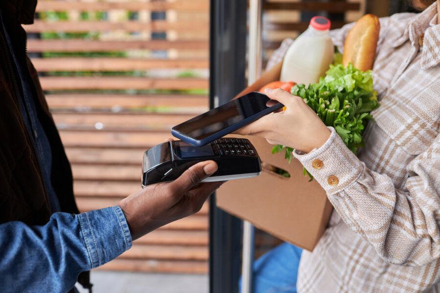 Close up of unrecognizable woman paying for grocery delivery via smartphone outdoors