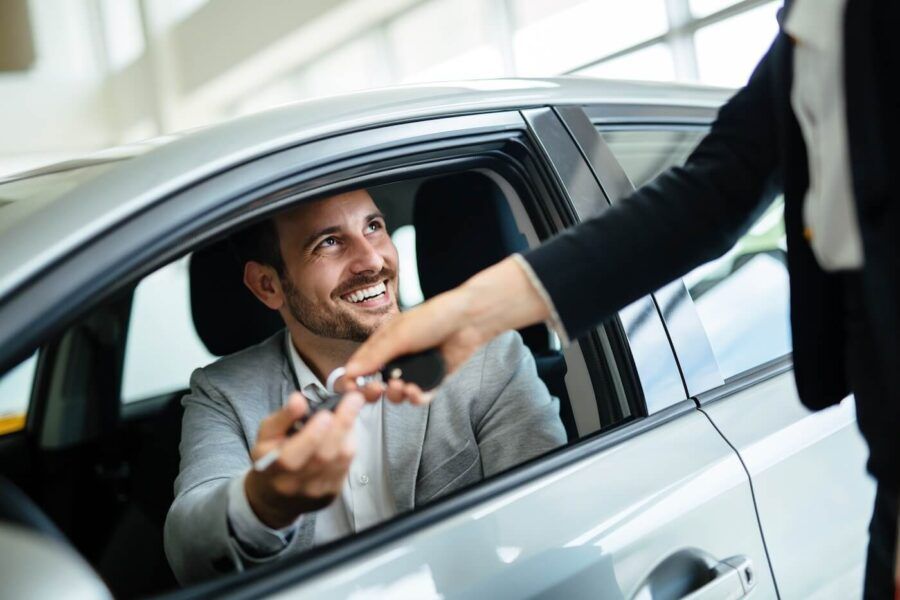 Sales agent giving the car keys to a smiling man who is sitting in his new vehicle