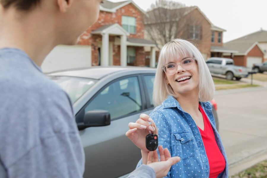 Smiling young woman in glasses giving the car keys to her friend