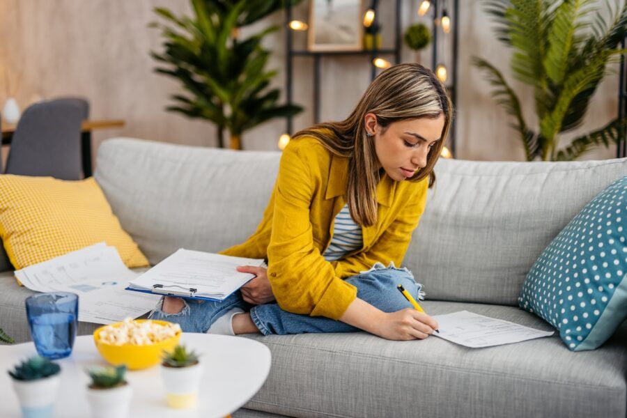 Young woman checking her finances while sitting on the sofa at home.
