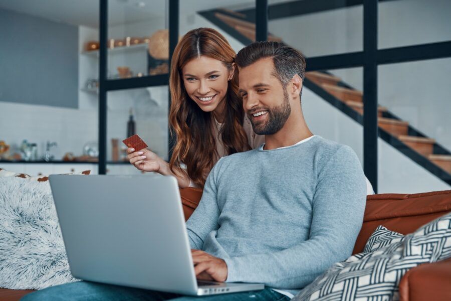 Cheerful young couple using laptop and smiling while renting a car online at home
