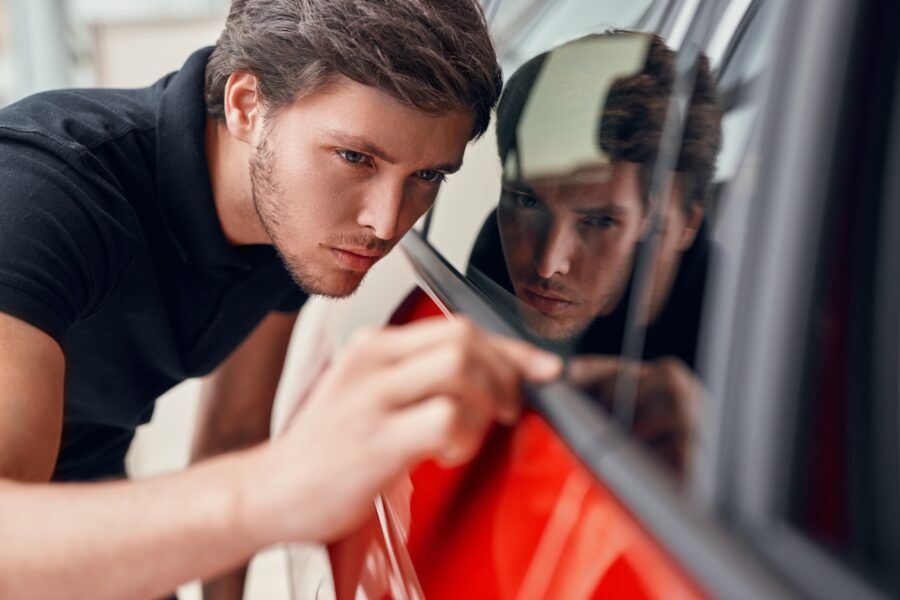 Male customer searching scratches on window of modern vehicle while choosing new car in showroom.