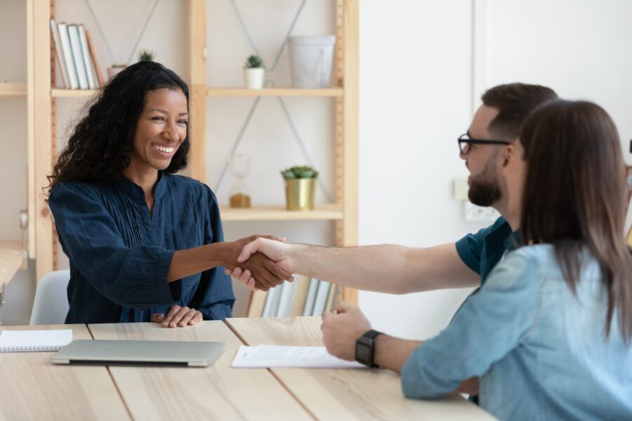 Real estate agent shaking hands with happy young couple in office at meeting.