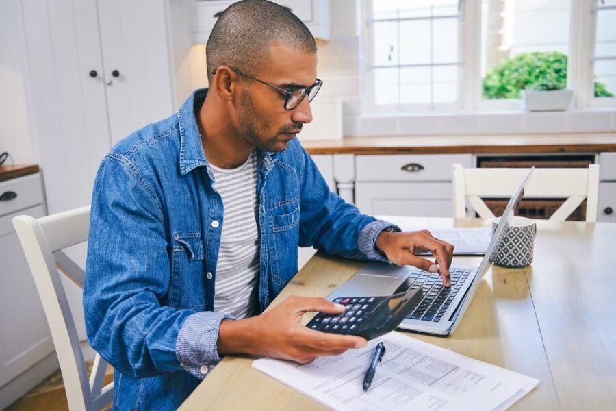 Young man using laptop and calculator in the kitchen