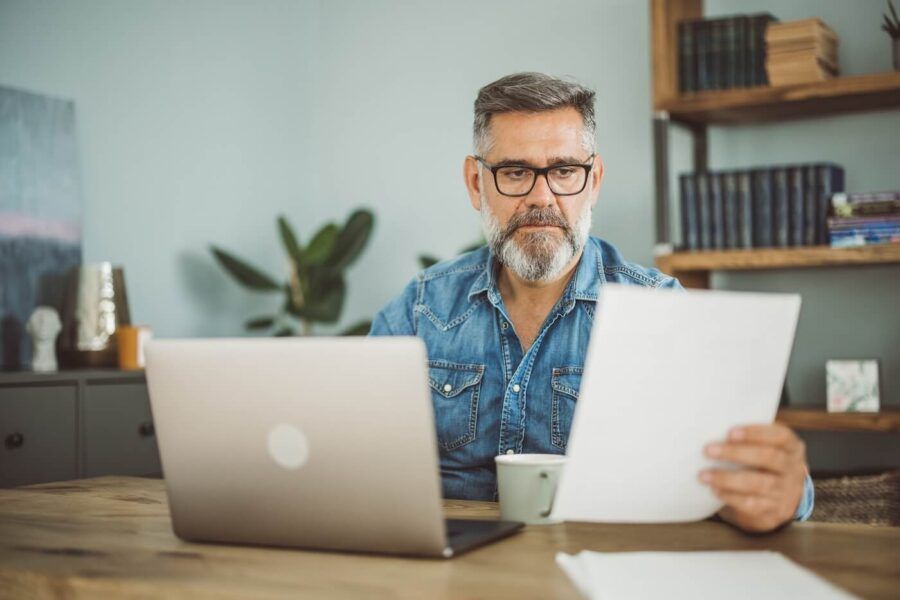 Mature man looking at the printout while using his laptop in a home office