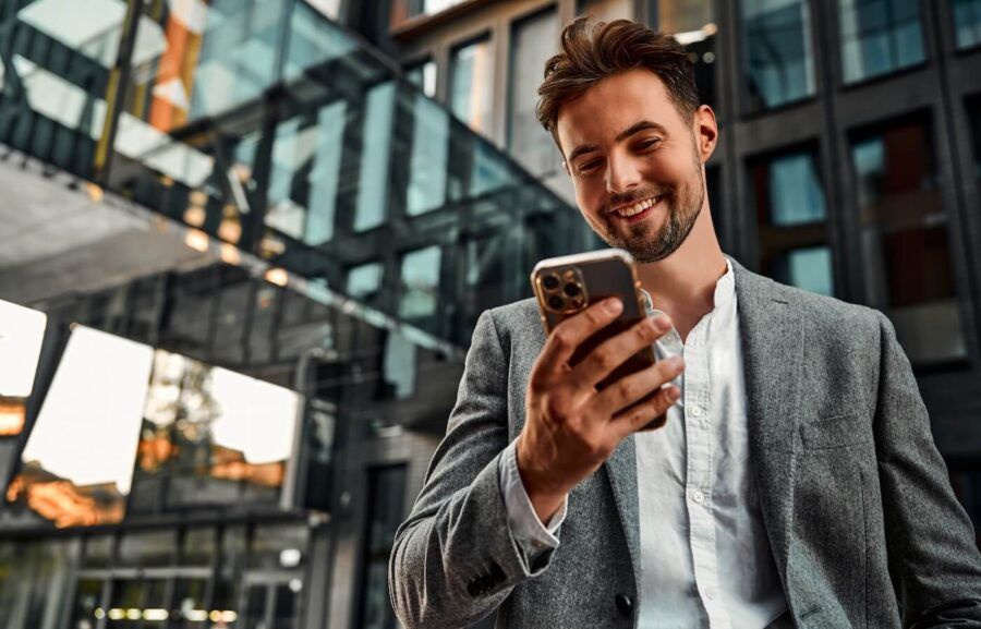 Smiling man checking his smartphone near the office building