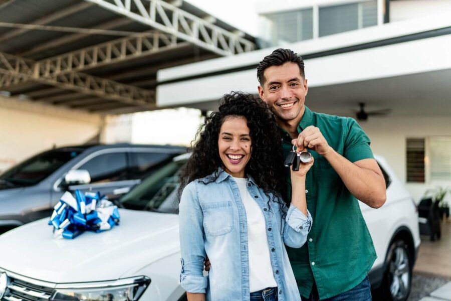 A happy couple standing next to their new car and holding the car keys