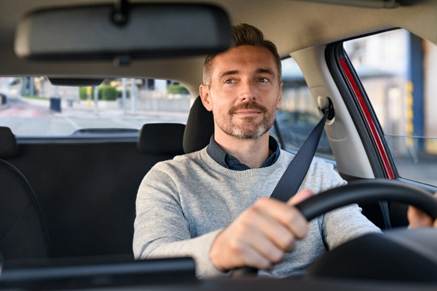 Mid adult casual man smiling while driving car and looking at mirror for reverse.