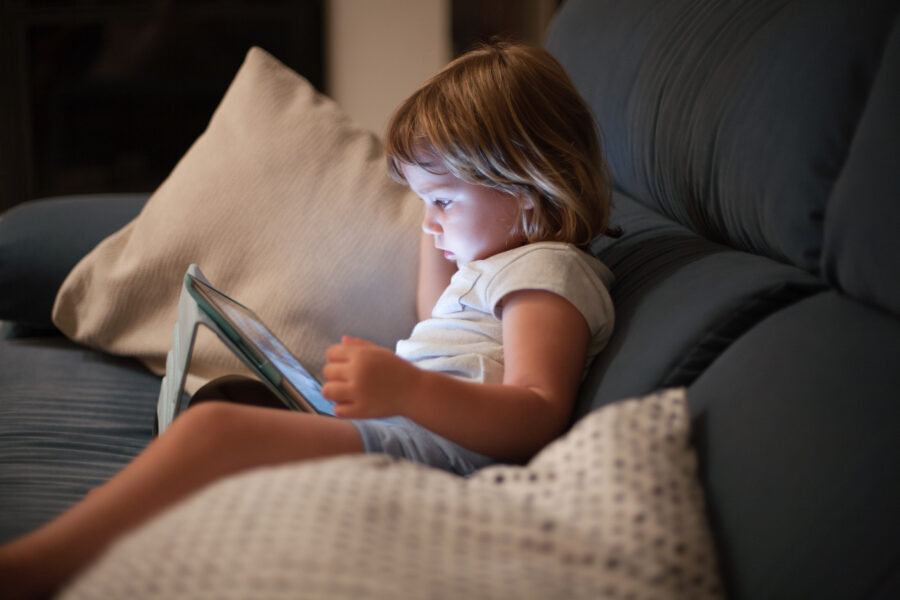little child sitting comfortably in sofa watching tablet