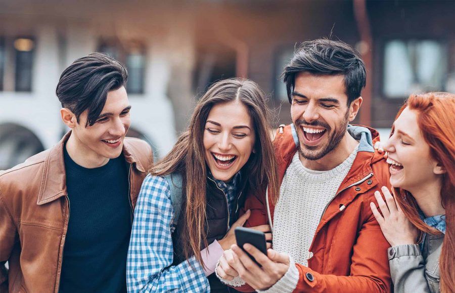 college student group of two boys and two girls laughing while looking at phone