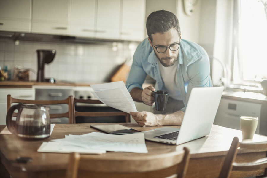 Concerned man holding coffee is reviewing his finances in the kitchen,