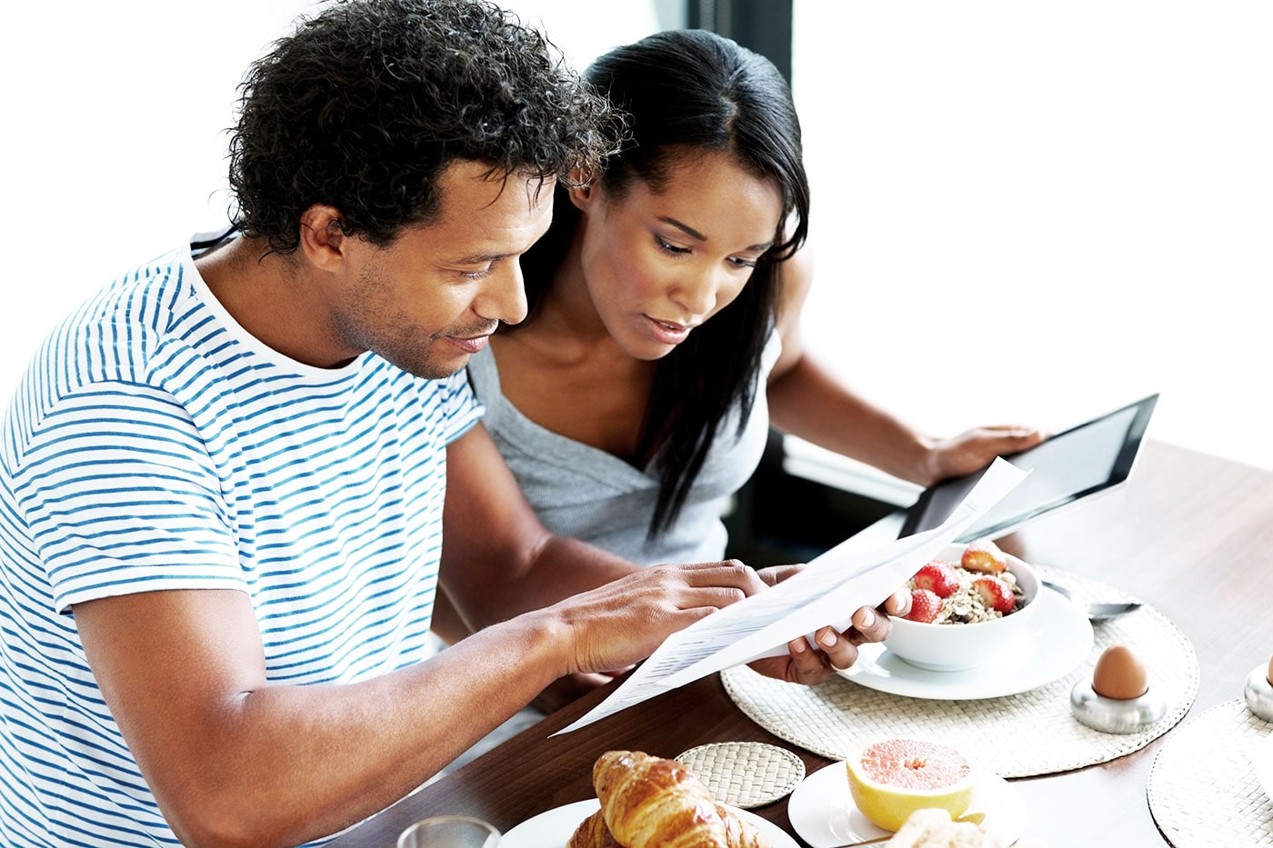 A couple having breakfast look at a document while holding a tablet.
