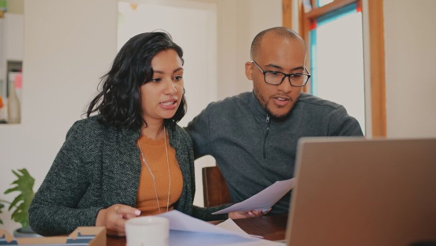 Shot of a young couple using a laptop reviewing whether or not to sell their life insurance policies.