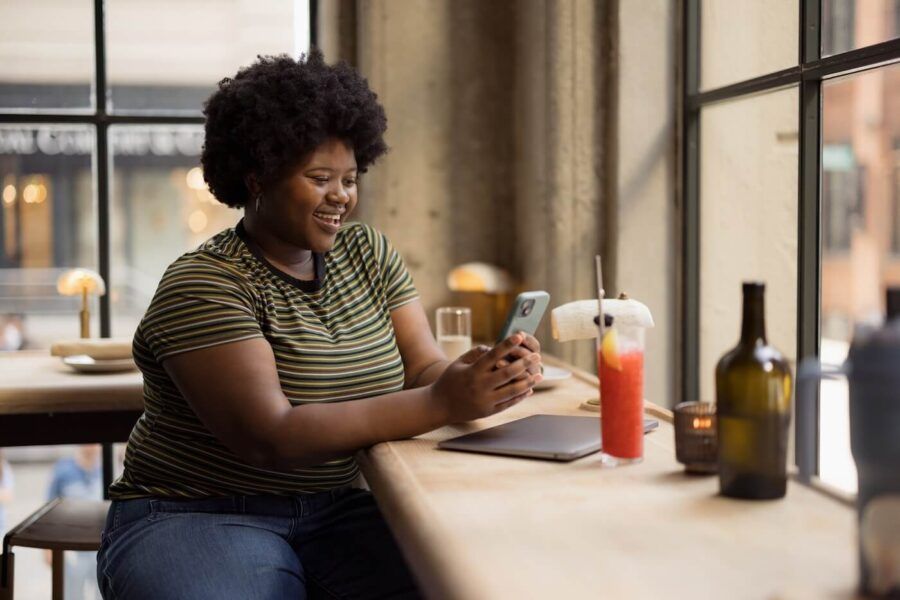 Smiling woman sitting in the cafe and reviewing her credit report on her smartphone