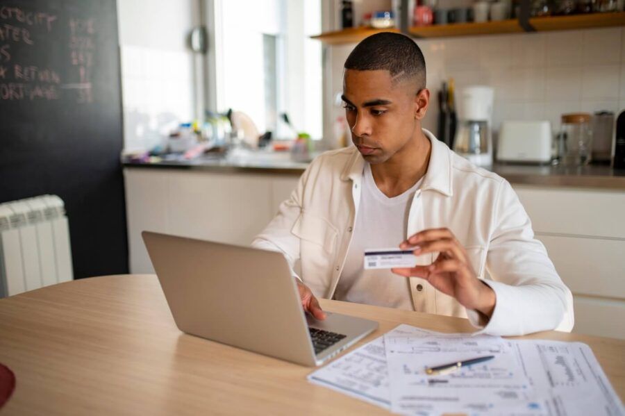Focused young man using his laptop and a credit card in the kitchen