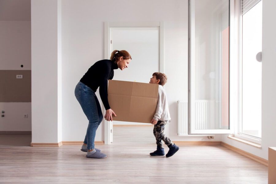 A young boy is helping his mother to carry a moving box into a new apartment