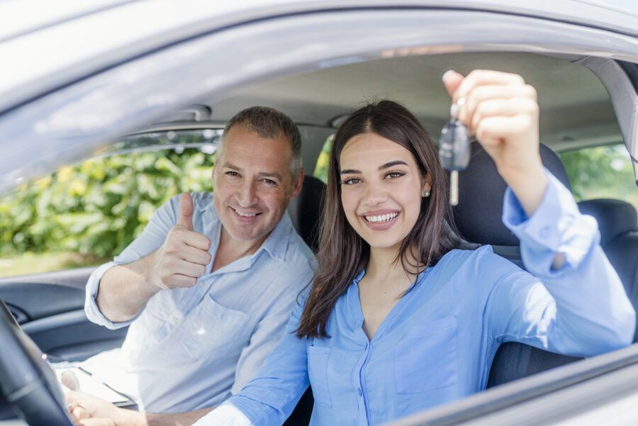 Daughter and father sitting in a car. The daughter is holding keys and smiling.