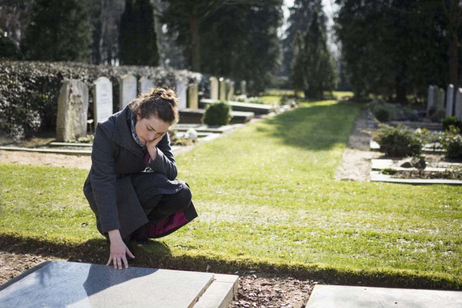 Woman sitting at grave with hand on grave