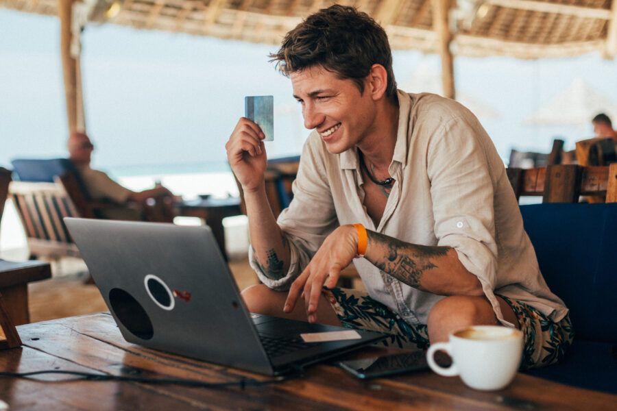 A young man making online payments with debit card and drinks coffee in a cafe on the beach.