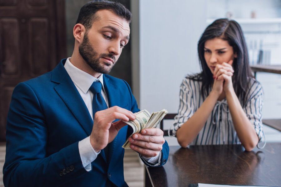 Debt collector counts money while a nervous woman watches with clenched hands