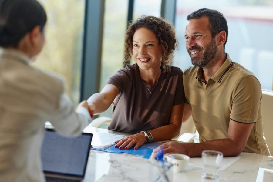 Smiling couple shaking hands with a female financial advisor in her office