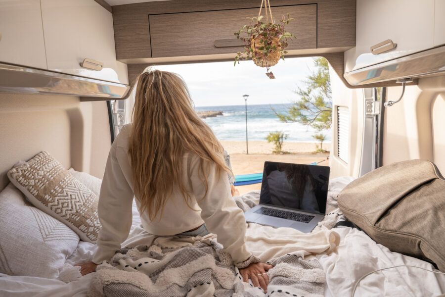 View of woman working on her laptop from the bed of her camper van parked at the beach.