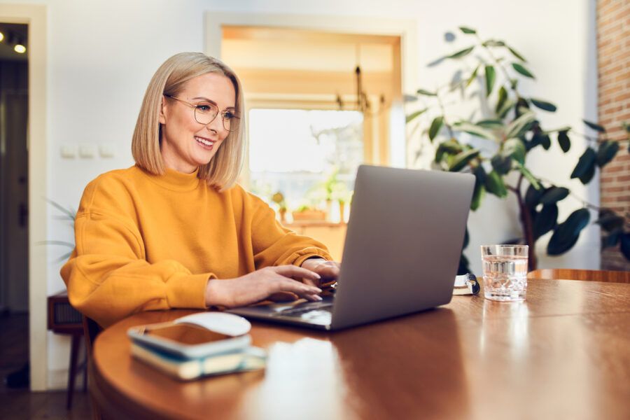 Portrait of middle aged woman sitting at dining table with laptop working at home