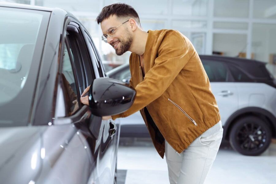 Smiling male customer looking inside a vehicle through the side window at a car dealership