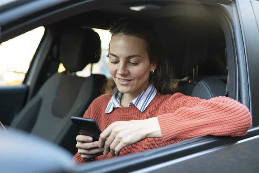 Smiling woman using smart phone while sitting inside of a parked car.