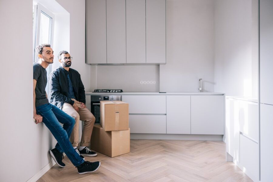 Candid male couple sitting in their new apartment, taking a break from moving.