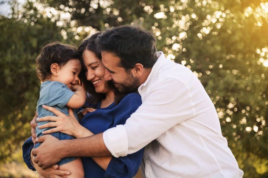 A happy family with a baby sharing a warm hug in a sunny park, surrounded by greenery