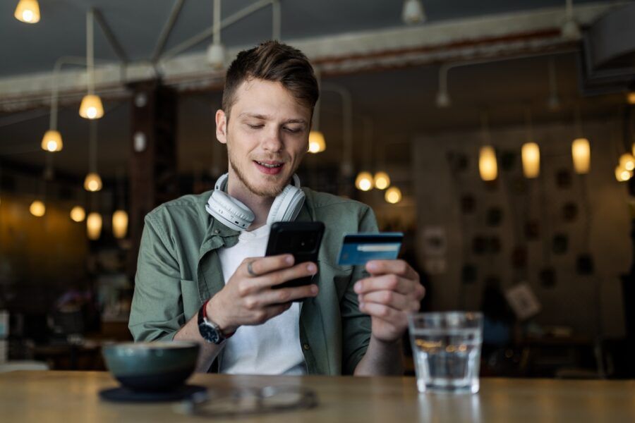 Happy Man holding Phone and Credit Card in cafe.