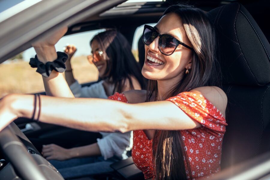 Shot of two young women singing while driving a car on road trip on beautiful summer day.