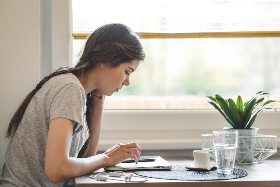 Young woman with braided hair sitting by the table, looking on her smart phone. Paying bills on the phone, checking her finance on the phone app.