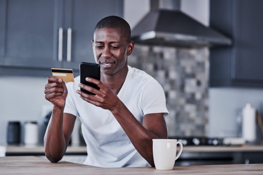 Shot of a young man using a mobile phone and credit card at home.