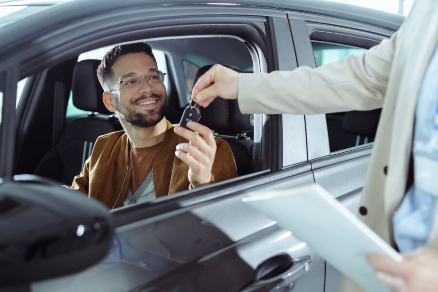 Happy man receiving keys for his new car as he sits in the driver's seat.